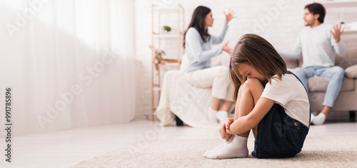 Family Conflict. Little girl crying after parents quarrel at home, sitting alone with her head down, hiding her face in knees, selective focus