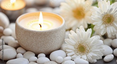 A serene setting with a lit candle surrounded by white stones and fresh flowers on a soft surface