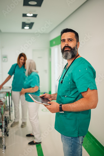 Male doctor with tablet in hospital hallway with colleagues.