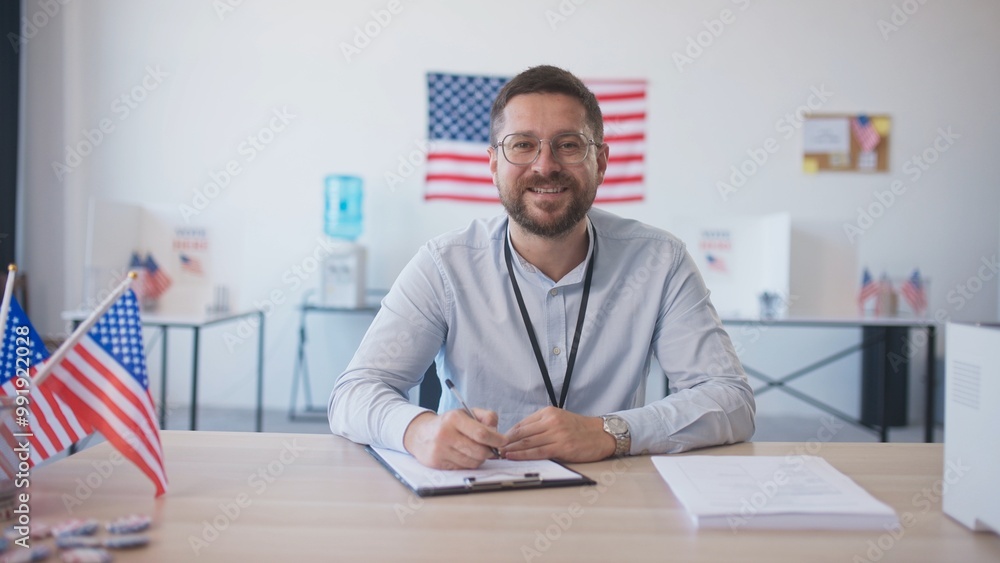 Camera moving closer to Caucasian male with beard and glasses sitting at desk. Finishing filling information on piece of paper. Using pen to write information. American flags in background. Camera moving closer to Caucasian male with beard and glasses sitting at desk. Finishing filling information on piece of paper. Using pen to write information. American flags in background.