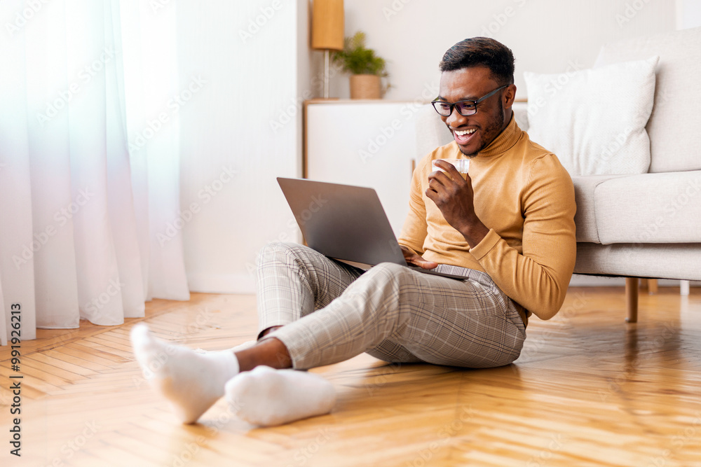 Freelance Lifestyle. Relaxed Afro Guy Working On Laptop Drinking Coffee Sitting On Floor Indoor. Selective Focus Freelance Lifestyle. Relaxed Afro Guy Working On Laptop Drinking Coffee Sitting On Floor Indoor. Selective Focus