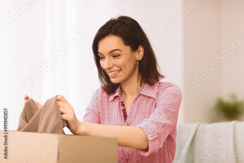 Donation Concept. Happy woman holding clothes, putting it in cardboard carton box with happy expression, copyspace Free Download Donation Concept. Happy woman holding clothes, putting it in cardboard carton box with happy expression, copyspace - GFXLoad