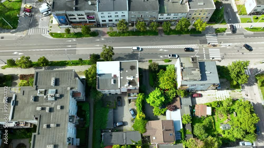 Aerial top-down view of a busy city street, with buildings on both sides, cars moving along the road, and residential homes with green gardens Aerial top-down view of a busy city street, with buildings on both sides, cars moving along the road, and residential homes with green gardens