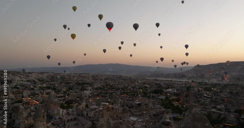 Drone ascends gradually past stone spire towers with green glow on horizon against silhouette of hot air balloons, Cappadocia Turkey Drone ascends gradually past stone spire towers with green glow on horizon against silhouette of hot air balloons, Cappadocia Turkey