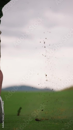 Golfer hitting wedge shot making big divot in slow motion, ball landing on green, vertical 4k golf footage