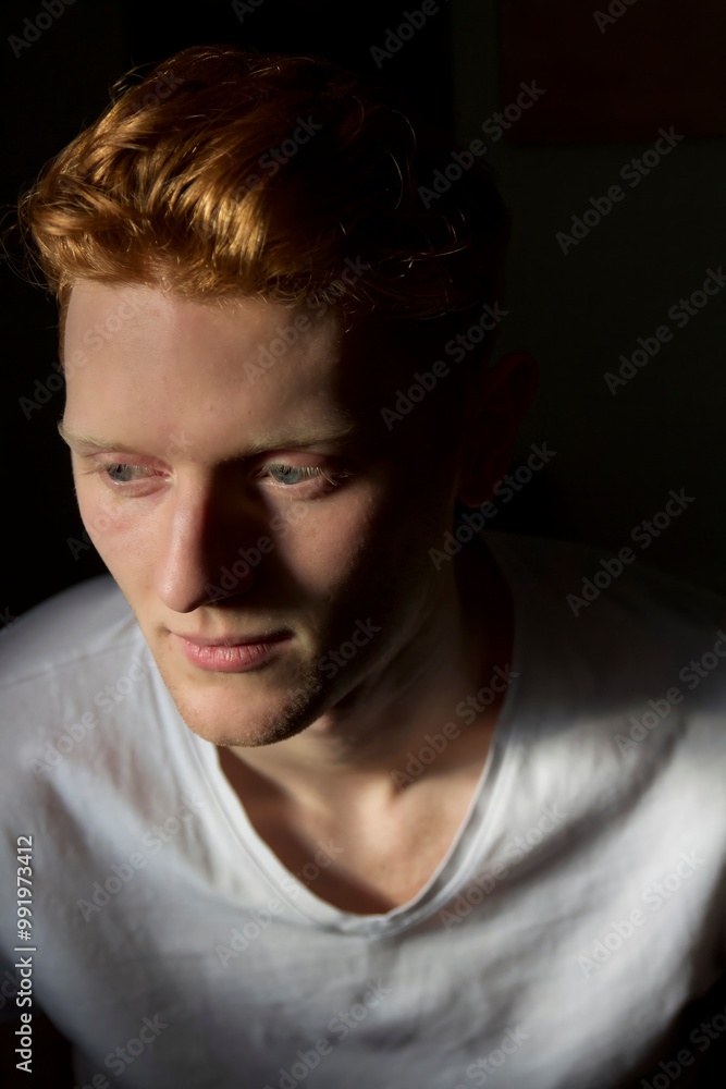 Young man with auburn hair sitting in dim light while deep in thought Young man with auburn hair sitting in dim light while deep in thought