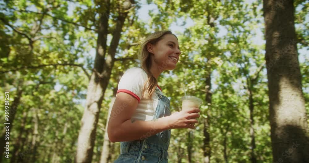 A Young Woman Delightedly Enjoying a Refreshing Drink in a Lush Forest Environment A Young Woman Delightedly Enjoying a Refreshing Drink in a Lush Forest Environment