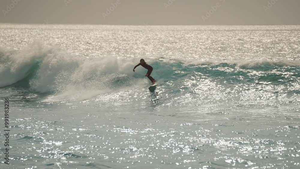 Male surfer riding the perfect ocean wave in slowmotion at golden sunset. Man in surfing suit catching the perfect wave in beautiful golden evening light. The setting sun is creating reflections. Male surfer riding the perfect ocean wave in slowmotion at golden sunset. Man in surfing suit catching the perfect wave in beautiful golden evening light. The setting sun is creating reflections.