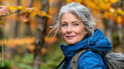 A woman with gray hair smiles while hiking in a colorful autumn forest with bright leaves