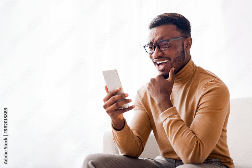 Happy Black Guy Holding Cellphone Texting Chatting Online Sitting On Couch Indoor. Modern Communication Happy Black Guy Holding Cellphone Texting Chatting Online Sitting On Couch Indoor. Modern Communication