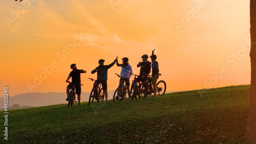 SILHOUETTE: Golden sunset and a group of mountain bikers celebrating on top of the hill after joyful uphill ride. Beautiful autumn day for cycling and exploring the scenic countryside with friends.