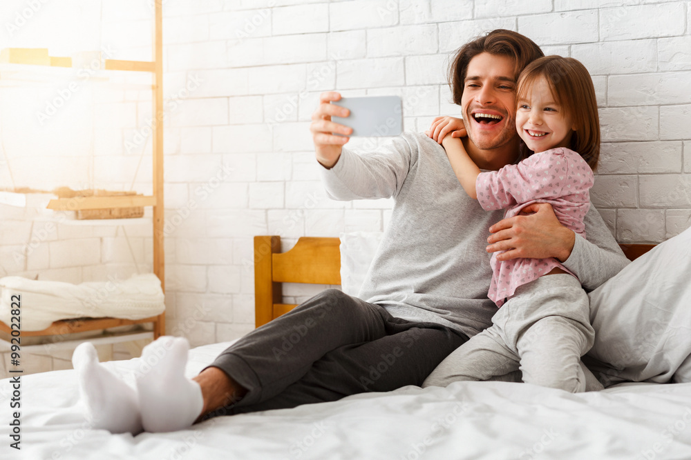 Happy preschool girl and father taking selfie on smartphone, laying on bed in morning, free space Happy preschool girl and father taking selfie on smartphone, laying on bed in morning, free space