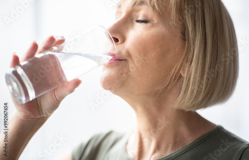 Portrait of sporty mature woman drinking water during her workout indoors. Fit mature lady staying hydrated after domestic sports training. Healthy lifestyle concept