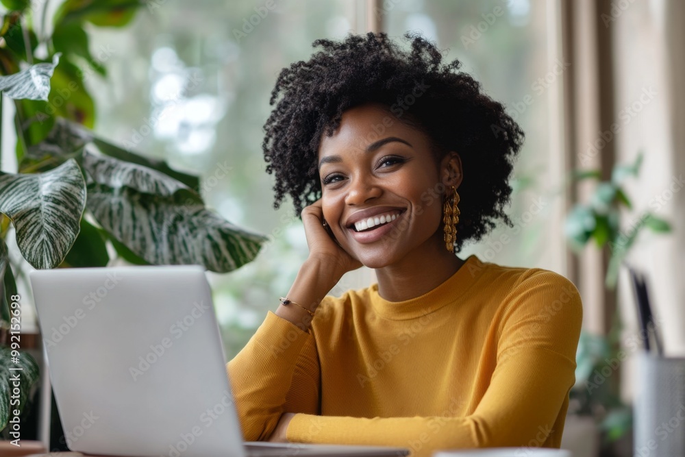 Young woman is sitting at her desk and smiling while working on her laptop Young woman is sitting at her desk and smiling while working on her laptop