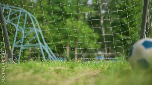 A soccer ball is kicked into a goal post as the goalkeeper misses the ball, on a grassy field with a blur background of outdoor equipment photo