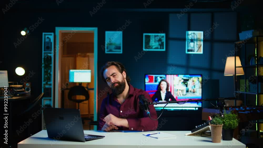 Joyful content creator sitting at table talking in microphone in dimly lit home studio interior, chatting with subscribers. Upbeat man surrounded by podcast recording gear in apartment, camera B Joyful content creator sitting at table talking in microphone in dimly lit home studio interior, chatting with subscribers. Upbeat man surrounded by podcast recording gear in apartment, camera B