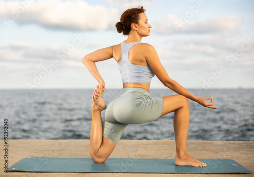 Example of performing hatha yoga asana. Amateur and professional girl doing yoga near sea, on embankment she fulfil crescent moon pose, Anjaneyasana photo