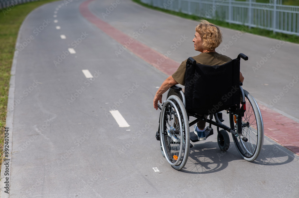 Rear view of an elderly woman in a wheelchair riding on a bike path. Rear view of an elderly woman in a wheelchair riding on a bike path.