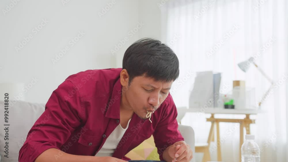 Asian attractive man eating instant noodles in living room at home. Asian attractive man eating instant noodles in living room at home.