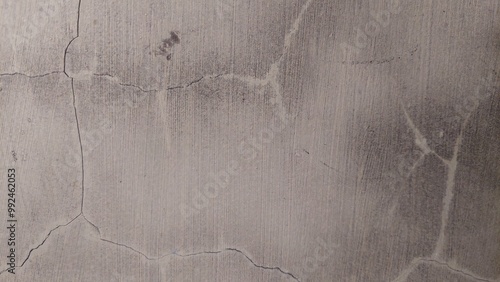 A close-up shot of a cracked concrete surface, revealing the underlying texture. The surface is pale gray with subtle shades of brown and white. The image is ideal for backgrounds, textures, or abstra