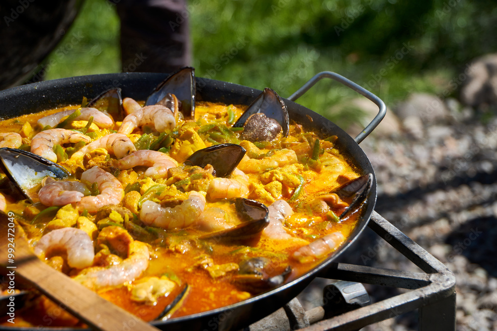 Close up while cooking a paella with vegetables, pork and seafood outdoors Close up while cooking a paella with vegetables, pork and seafood outdoors