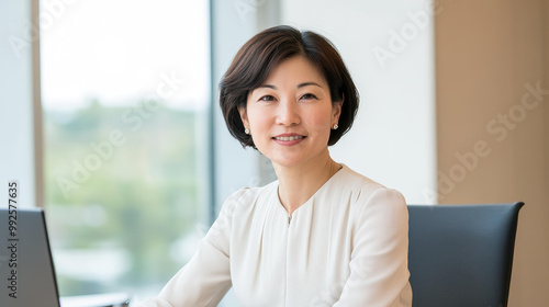 A cheerful Japanese woman in her s smiles while working on her laptop in a bright, modern office setting. Free Download A cheerful Japanese woman in her s smiles while working on her laptop in a bright, modern office setting. - GFXLoad