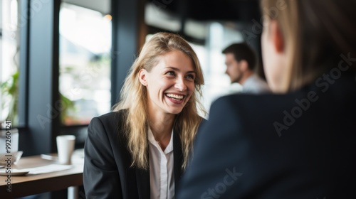 A cheerful businesswoman in a lively conversation, sharing a moment of camaraderie with her colleague in a modern office setting.