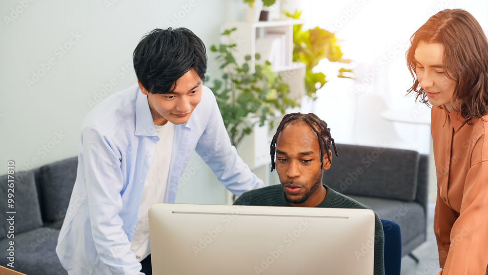 Multinational people in casual wear having a meeting about business management while looking at a computer in an office Multinational people in casual wear having a meeting about business management while looking at a computer in an office