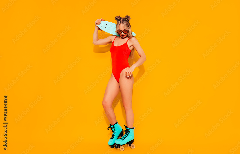 Young smiling blond model in summer swimwear bathing suit. Sexy carefree woman having fun. Hot female isolated on yellow wall in studio. Cheerful and happy, riding quad rollers, full length Young smiling blond model in summer swimwear bathing suit. Sexy carefree woman having fun. Hot female isolated on yellow wall in studio. Cheerful and happy, riding quad rollers, full length