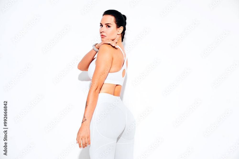 Portrait of fitness confident woman in white sports clothing. Sexy young beautiful model with perfect body. Female isolated on white wall in studio. Stretching out before training Portrait of fitness confident woman in white sports clothing. Sexy young beautiful model with perfect body. Female isolated on white wall in studio. Stretching out before training