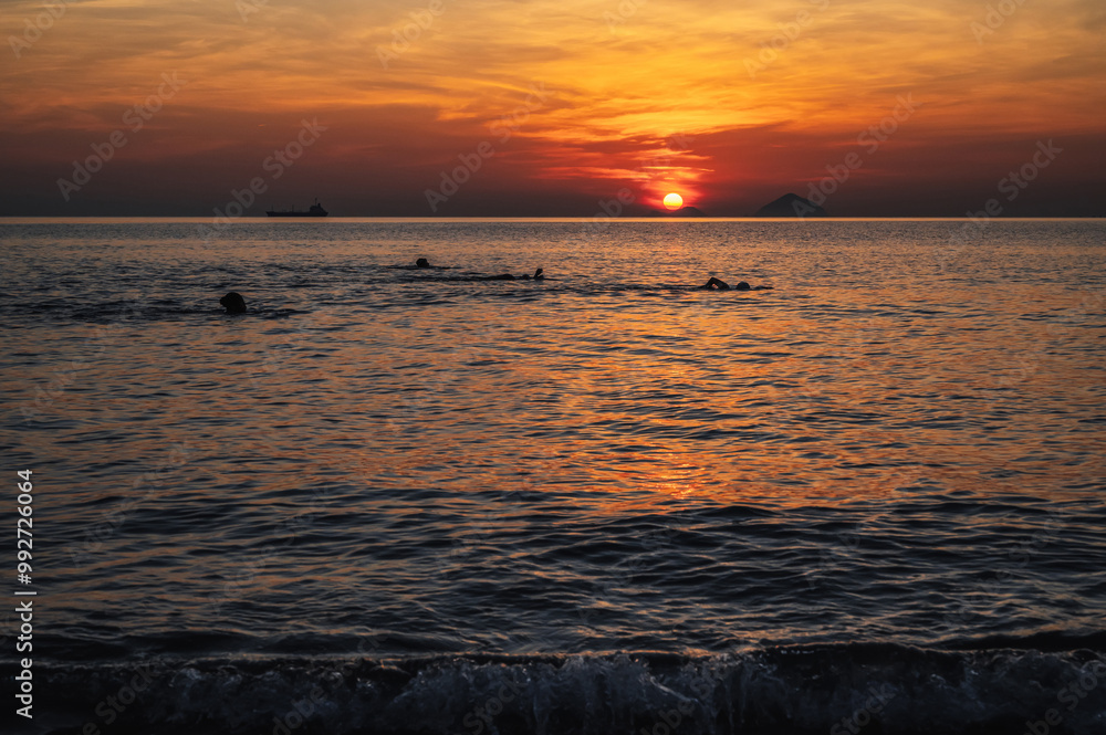 Silhouettes of people swimming in the sea at sunrise in the morning on vacation at a resort in summer Silhouettes of people swimming in the sea at sunrise in the morning on vacation at a resort in summer