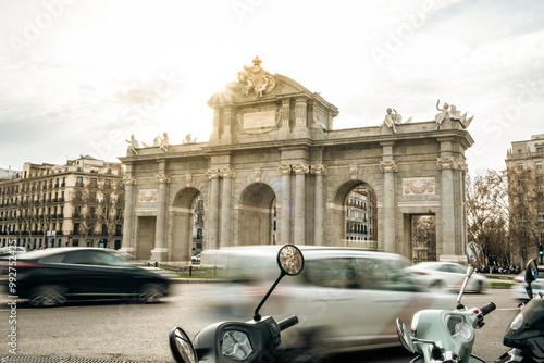 Alcala Door (Puerta de Alcala) ancient monument in the Independence Square in Madrid. Landmark of the city Madrid with glare of the sun and motion blurred cars and buses