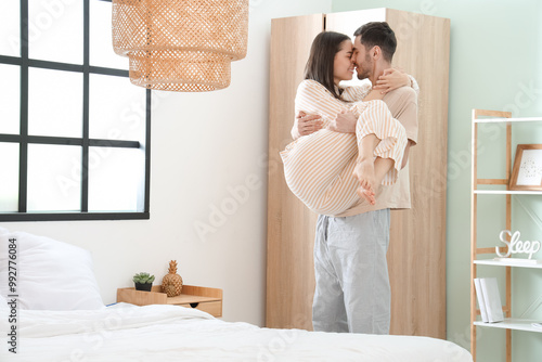 Φωτογραφία Young man holding his girlfriend on hands in bedroom