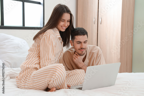 Lovely young couple with laptop on bed