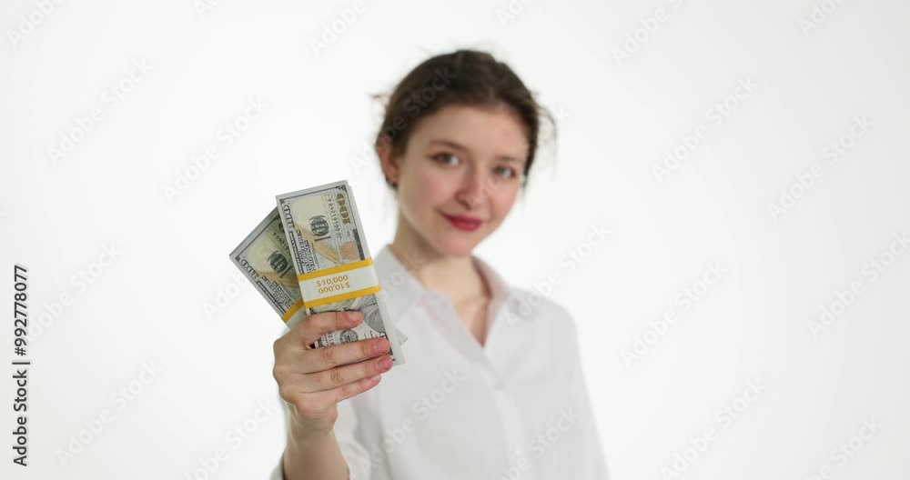 Positively smiling woman shows stacks of dollar banknotes in hand looking in camera slow motion. Young employee with monetary reward for productive work Positively smiling woman shows stacks of dollar banknotes in hand looking in camera slow motion. Young employee with monetary reward for productive work