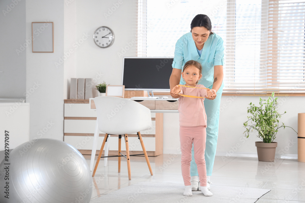 Female osteopath and little patient with elastic band doing exercises in clinic Female osteopath and little patient with elastic band doing exercises in clinic