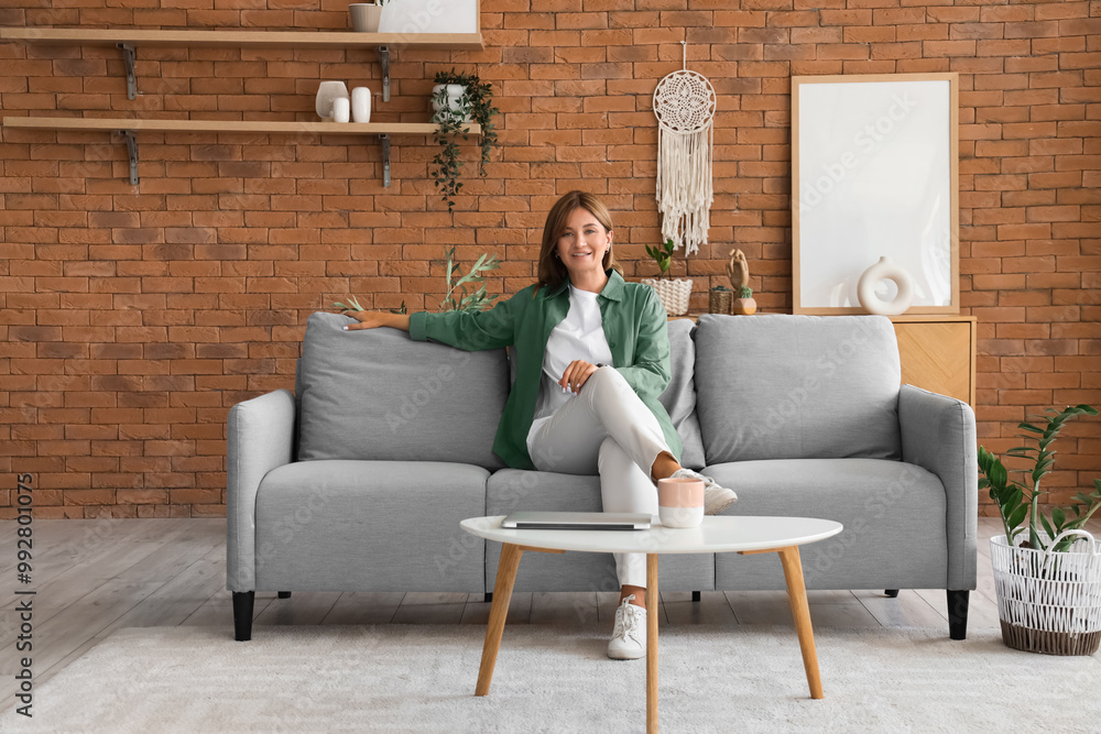 Beautiful woman sitting on grey sofa at home Beautiful woman sitting on grey sofa at home