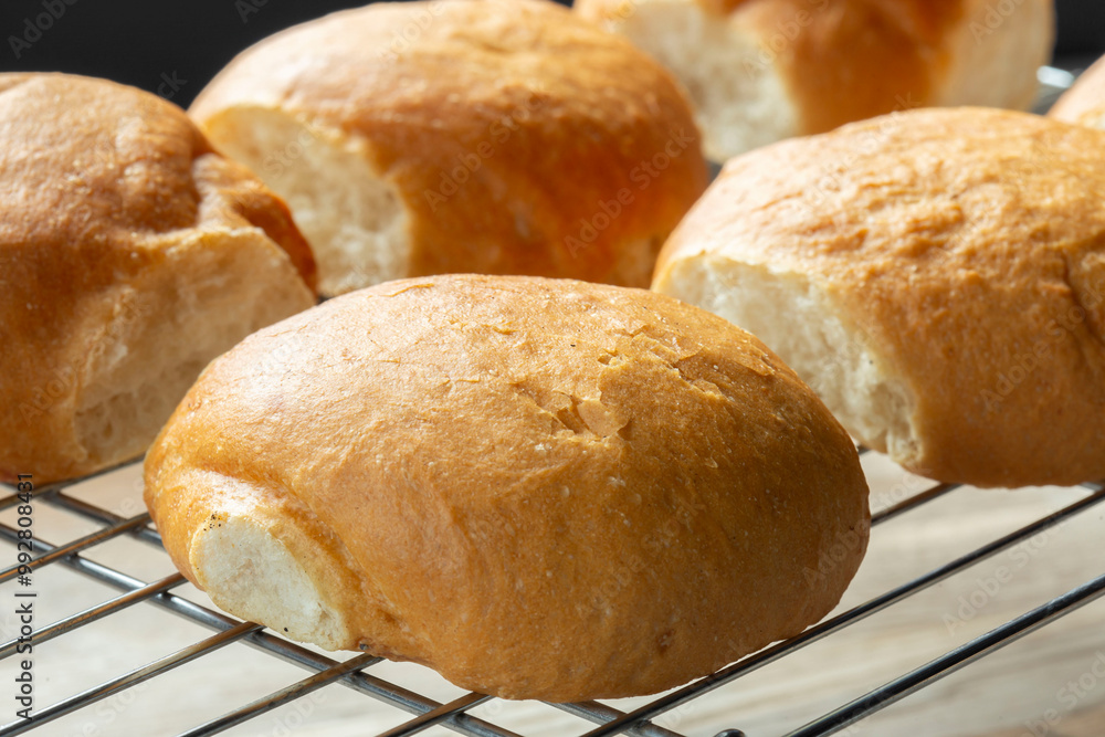 Freshly baked bread rolls cobs cooling down on a cooling rack on a wooden board. Home baking concept Freshly baked bread rolls cobs cooling down on a cooling rack on a wooden board. Home baking concept
