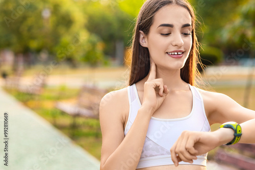 Sporty young woman counting pulse after training in park