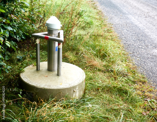 groundwater monitoring station in concrete base with protective stainless steel guard, side view