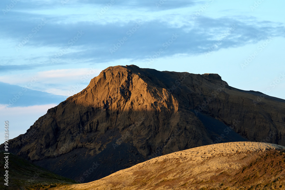 Rocky mountain with sunlight on ridge against cloudy blue sky Rocky mountain with sunlight on ridge against cloudy blue sky
