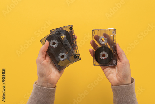 Two retro audio cassettes in female hands on yellow background. Close-up of hands with an audio cassette on a flat background, capturing retro vibes and nostalgia for phonotheques