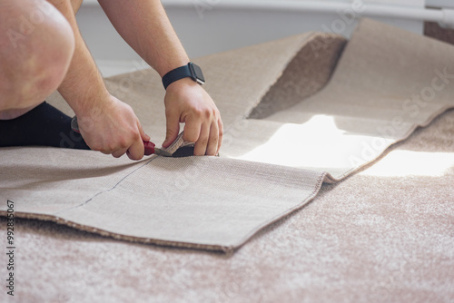 Male hands cutting carpet with blade during apartment renovation. Man in action during apartment repair, focused on cutting and fitting carpet professionally