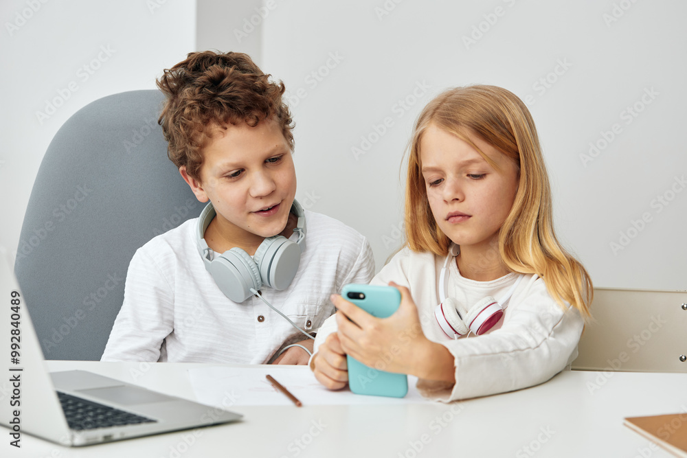Happy children enjoying online learning with laptops and headphones in the comfort of their home The two siblings, a boy and a girl, are sitting at a table in the cozy living room, fully engaged in Happy children enjoying online learning with laptops and headphones in the comfort of their home The two siblings, a boy and a girl, are sitting at a table in the cozy living room, fully engaged in