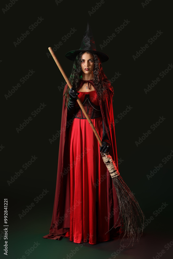 Fototapeta premium Young witch with broom on dark background