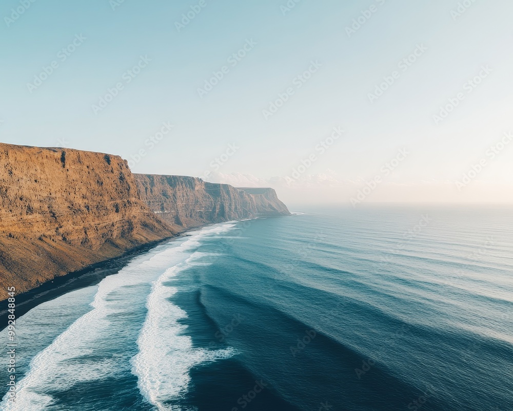 Aerial view of a dramatic coastline with rocky cliffs and crashing waves. The clear blue sky and ocean create a sense of tranquility and vastness. Aerial view of a dramatic coastline with rocky cliffs and crashing waves. The clear blue sky and ocean create a sense of tranquility and vastness.