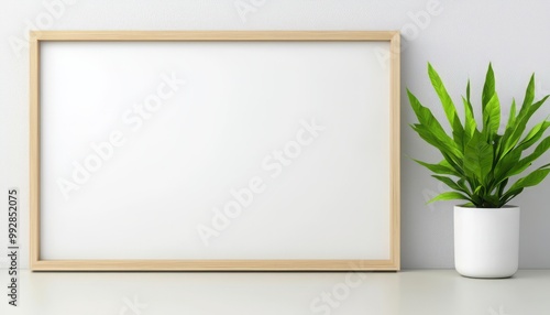 Minimalist interior scene featuring a blank frame and a potted plant on a clean white table against a light wall.