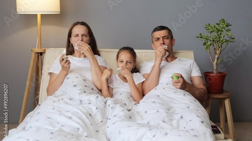 Sick tired ill unhealthy family lying together in bed coughing and experiencing sore throat using tissues and oral spays treating flu illness in cozy bedroom photo