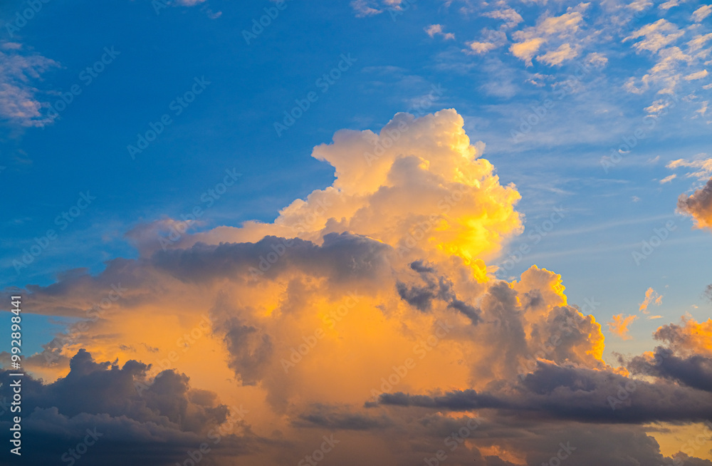 Fluffy clouds glow with warm golden light against a vibrant blue sky, creating a stunning and peaceful scene that captures the beauty of nature’s ever-changing canvas.