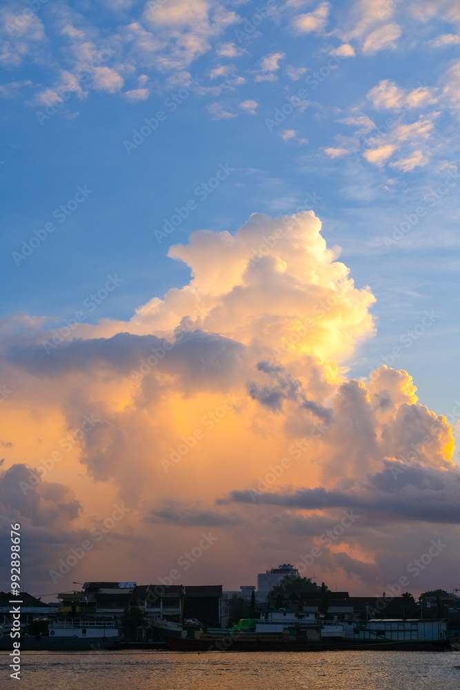 Sunset over Pontianak cityscape at Kapuas River’s edge, with vibrant blue and orange clouds reflecting on the water, capturing the serene beauty of the riverside city.